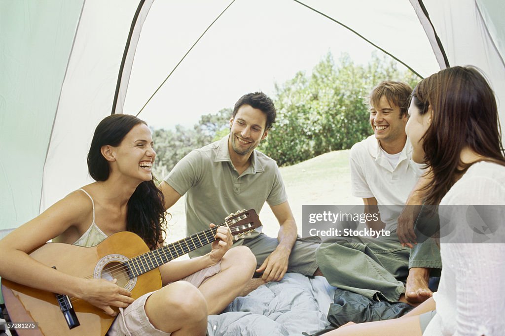 Young woman sitting with her friends and playing guitar inside a tent