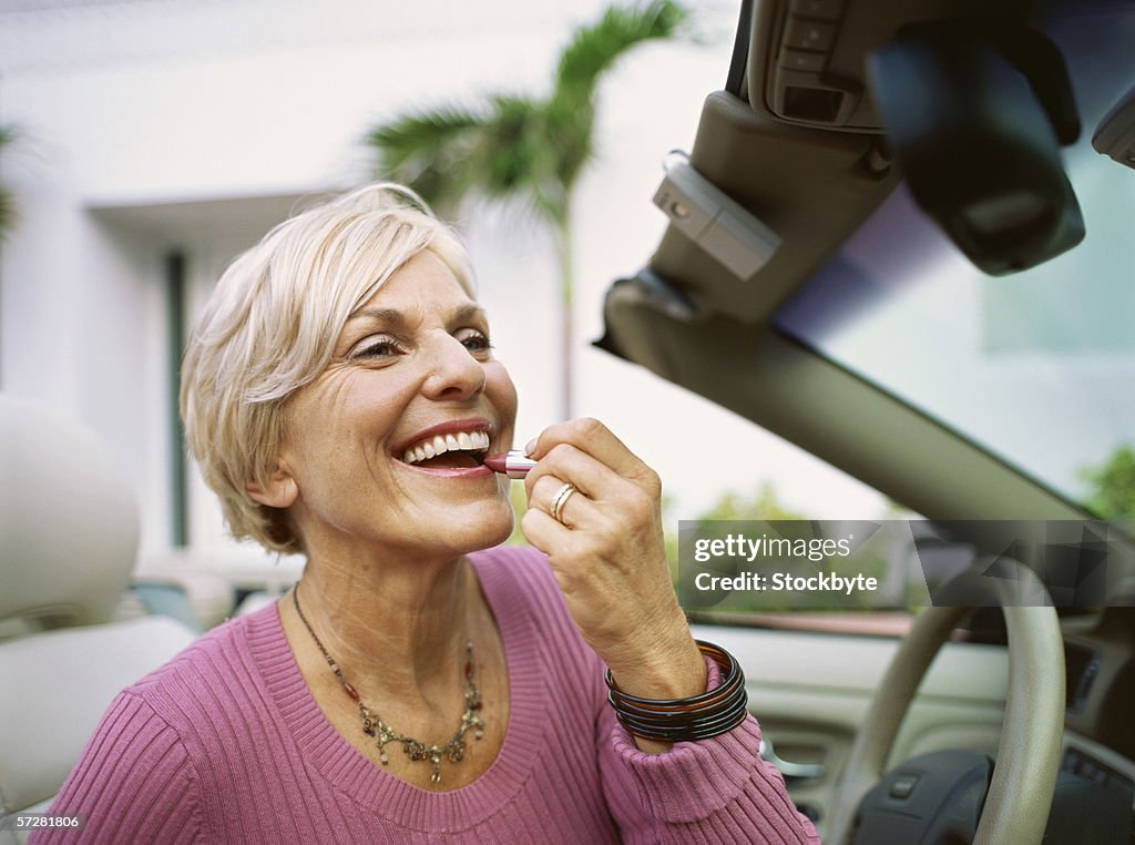 Close-up of a mature woman applying lipstick in car mirror