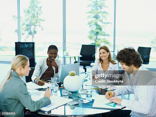 three businesswomen and a businessman sitting in an office at a round table - round table stockfoto's en -beelden