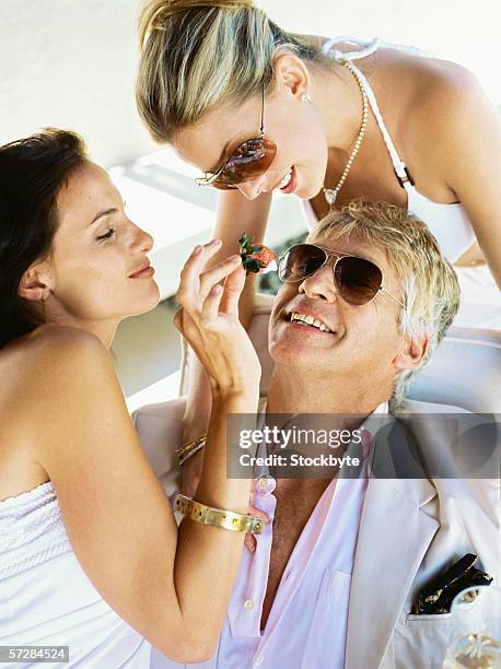 two young women feeding a mid adult man - sugar daddies stock pictures, royalty-free photos & images