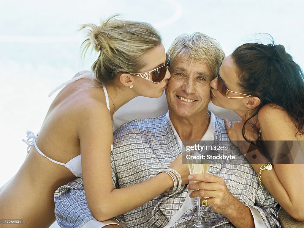 Two young women kissing a mid adult man