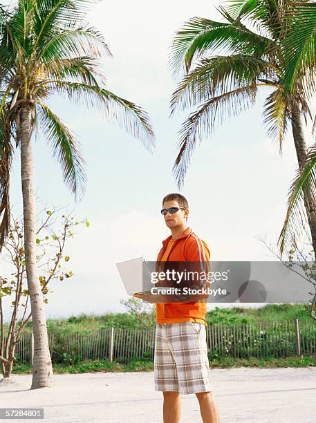 young man walking on the beach, holding a laptop - pantacourt photos et images de collection