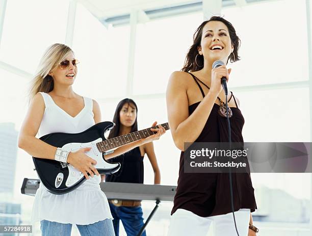 young woman singing with two young women playing musical instruments - girl band stock pictures, royalty-free photos & images