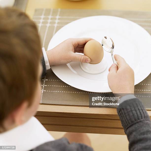 young boy (8-10) cracking a hard boiled egg with a spoon - kid boiled egg bildbanksfoton och bilder