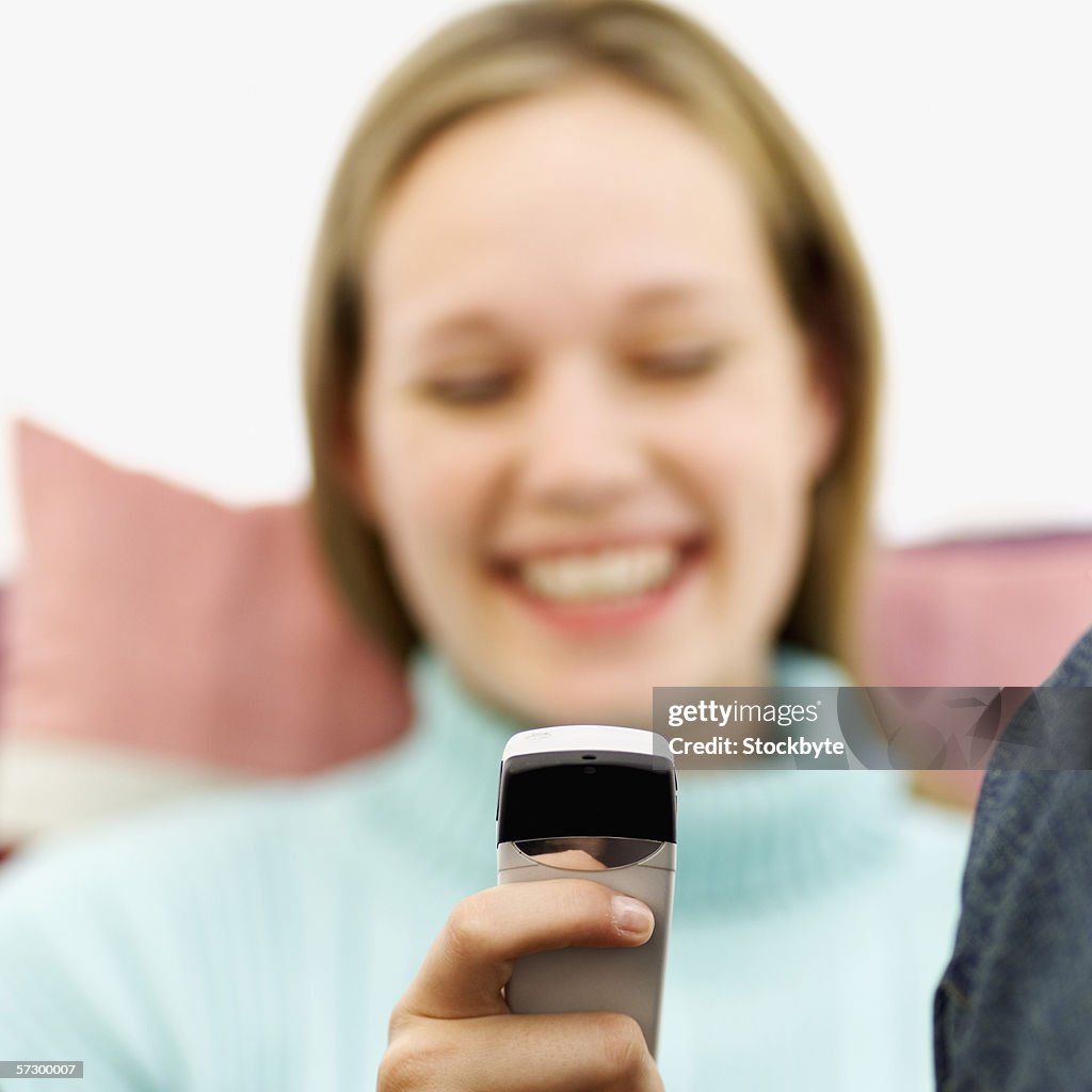 Close-up of a young woman sitting on a couch operating a mobile phone smiling (blurred)