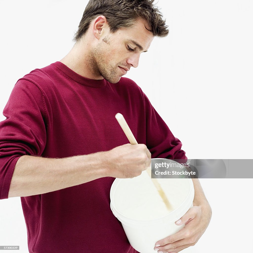 Young man mixing wallpaper glue in a bucket with a wooden stick