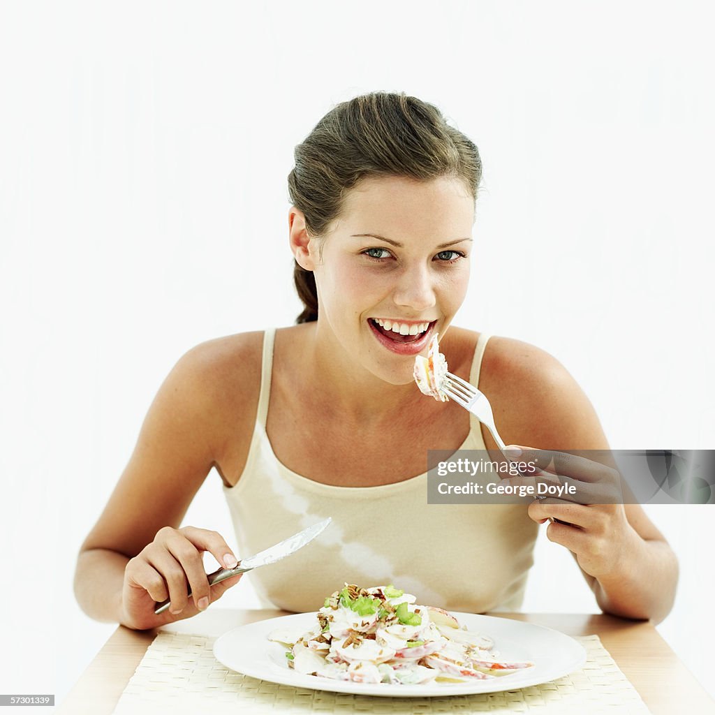 Portrait of a young woman eating apple salad with a fork