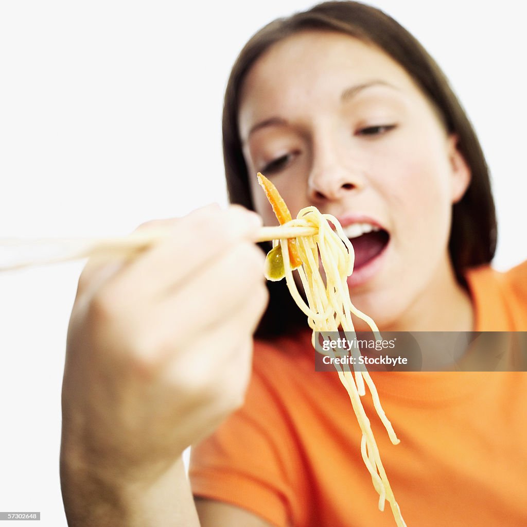 Close-up of a teenage girl (15-17) eating noodles with chopsticks (blurred)