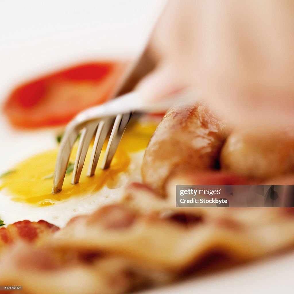 Close-up of a fork and knife cutting into a fried egg