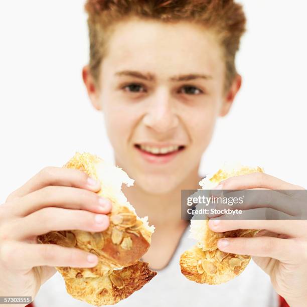 teenage boy (15-17) breaking a croissant into two (blurred) - breaking croissant stock pictures, royalty-free photos & images