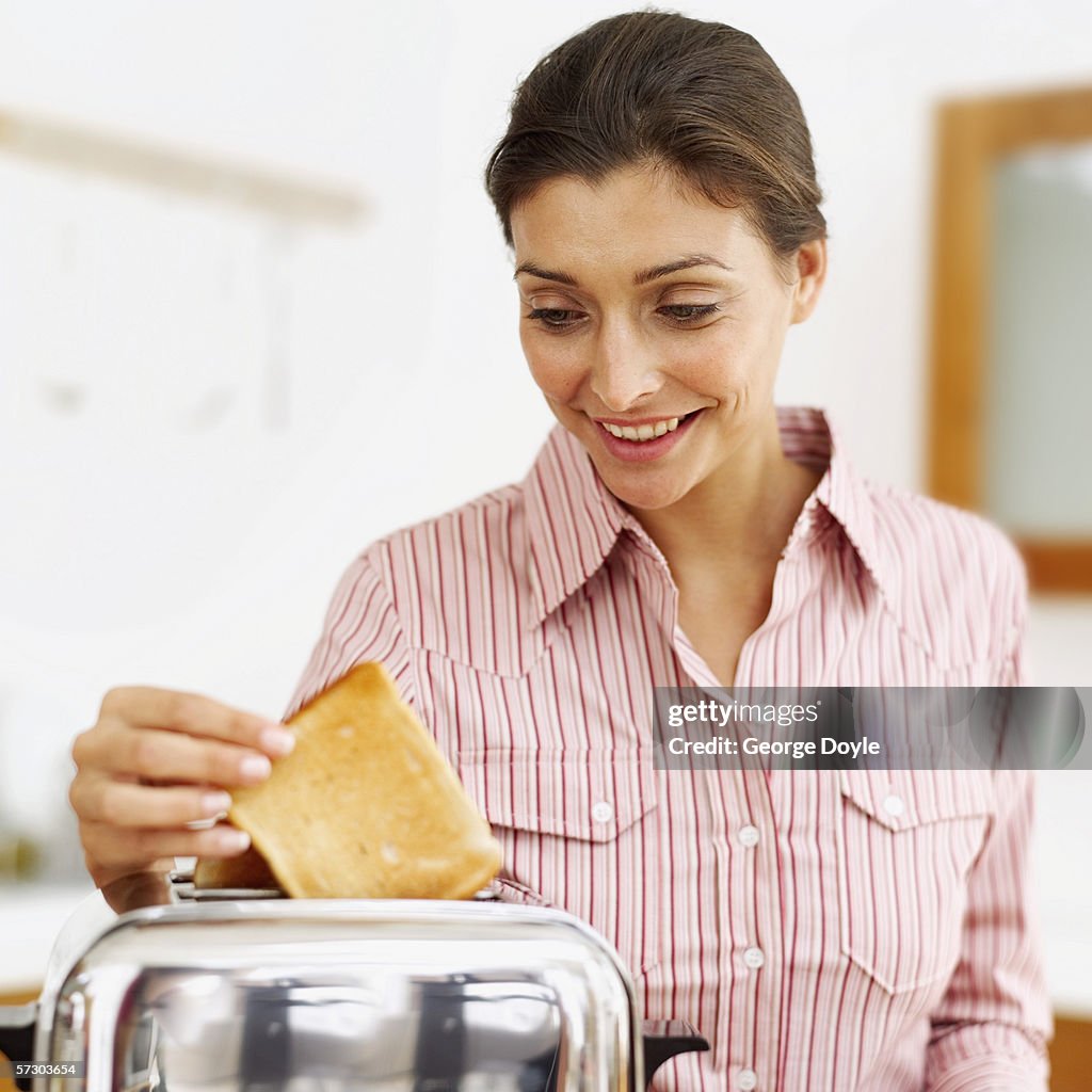 Young woman removing a slice of toast from an electric toaster