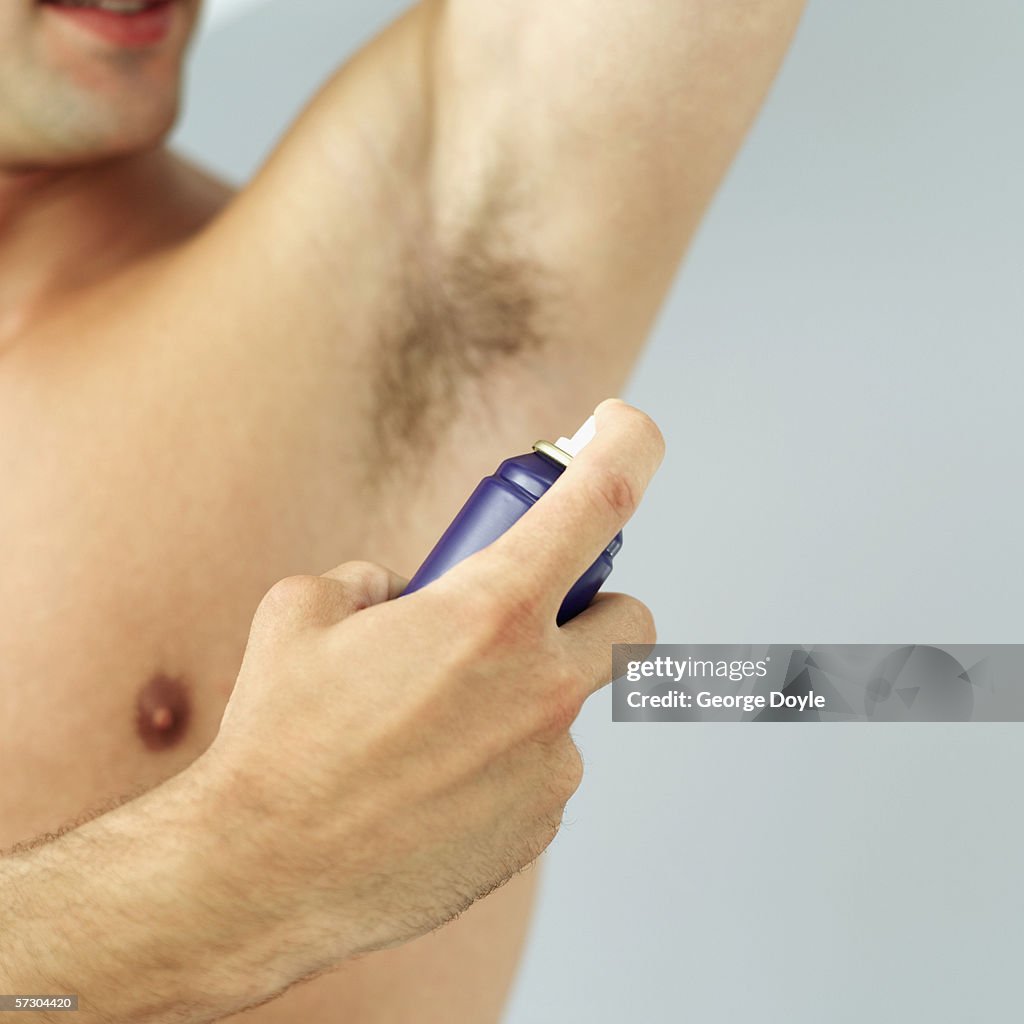 Close-up of a young man spraying his armpits with deodorant