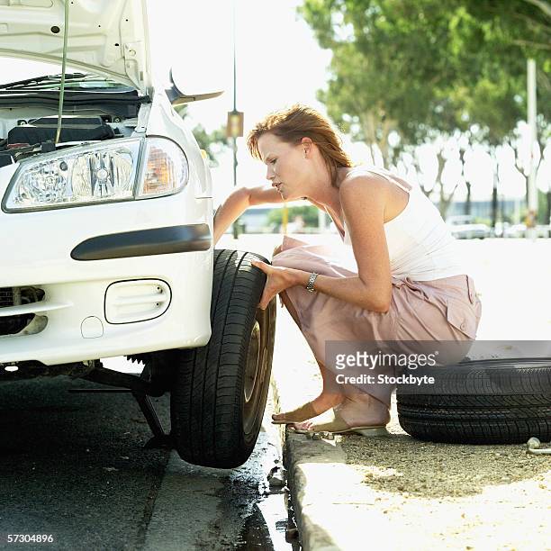 young woman changing a flat tyre - flat tyre stockfoto's en -beelden