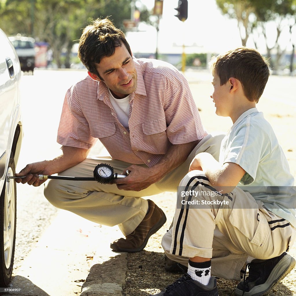 Young man checking the air pressure of car tire with his son