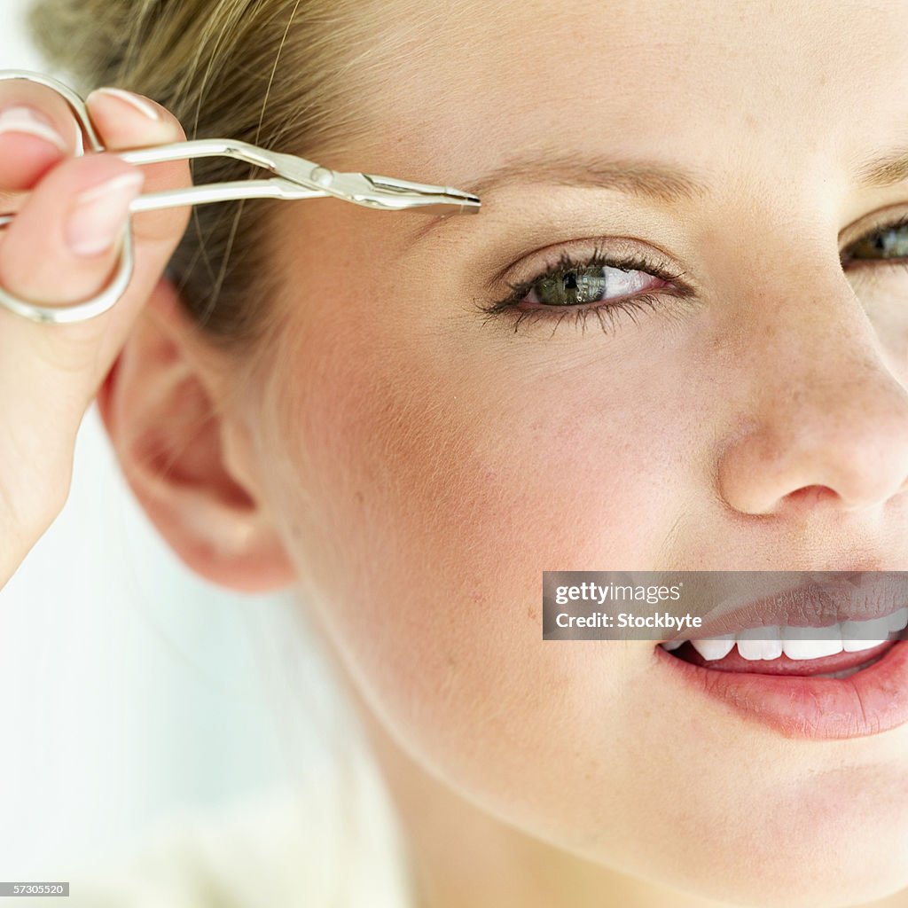 Close-up of a young woman tweezing her eyebrows