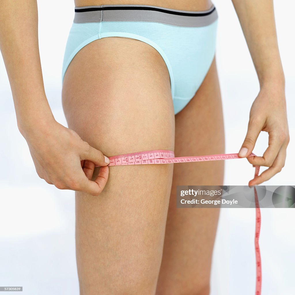 Mid section view of a young woman measuring her thigh with a measuring tape