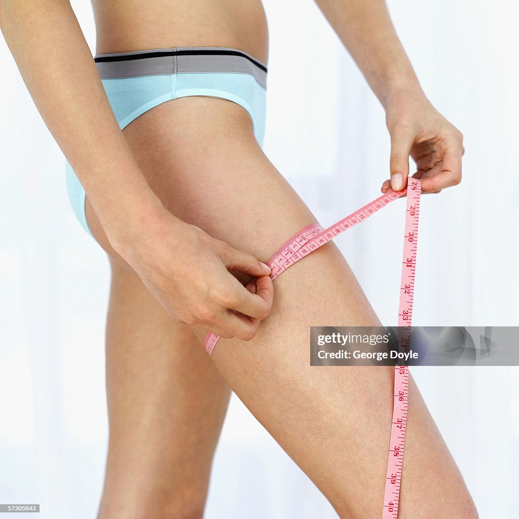 Woman measuring her thigh with a measuring tape