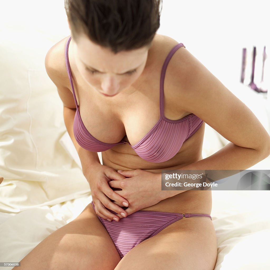 Young Woman Sitting On The Edge Of A Bed Wearing Underwear And Holding Her  Stomach High-Res Stock Photo - Getty Images