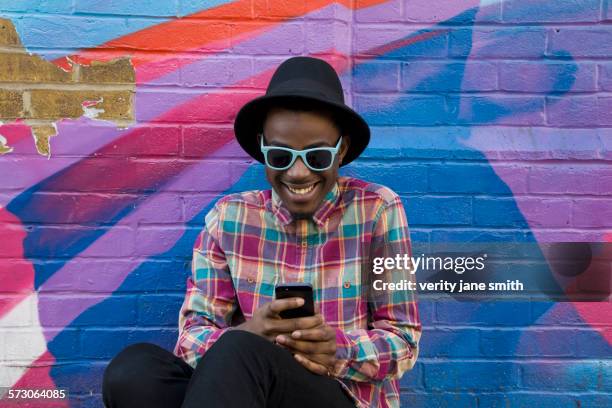 black man using cell phone near colorful wall - holding sunglasses photos et images de collection