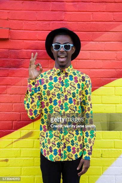 Black man in sunglasses making okay sign near colorful wall