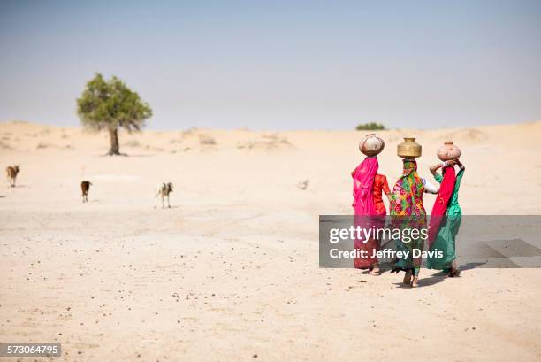 women carrying water in traditional baskets in remote desert - sand art in india stock-fotos und bilder