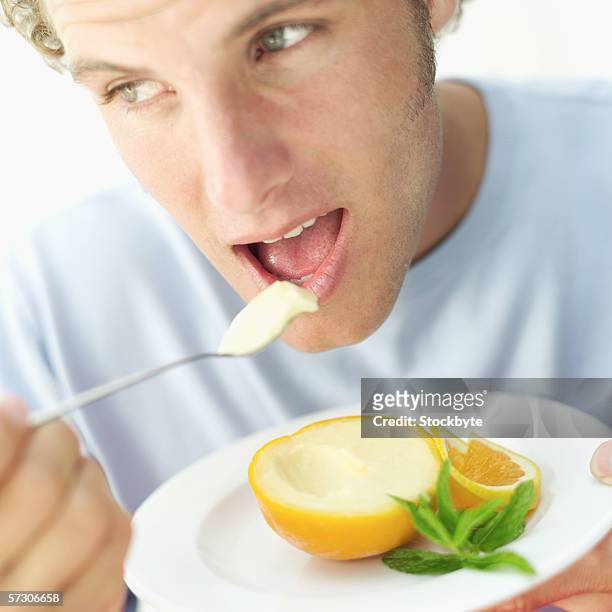 close-up of a young man eating orange sorbet with a spoon - orange sorbet stock pictures, royalty-free photos & images
