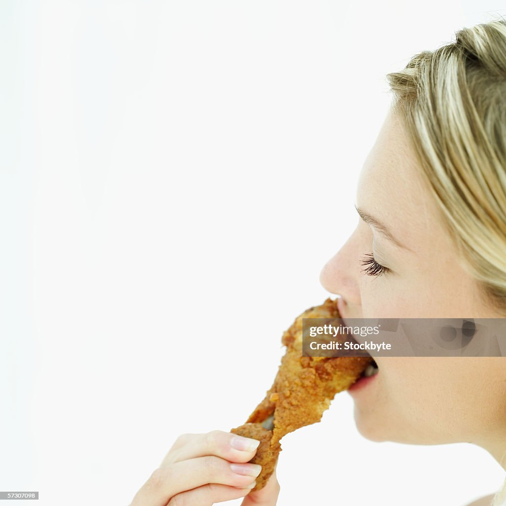 Side profile of a young woman eating a fried chicken drumstick