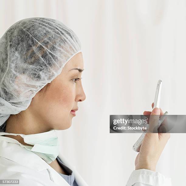 side profile of a female surgeon looking at a mobile phone - surgical mask profile stock pictures, royalty-free photos & images