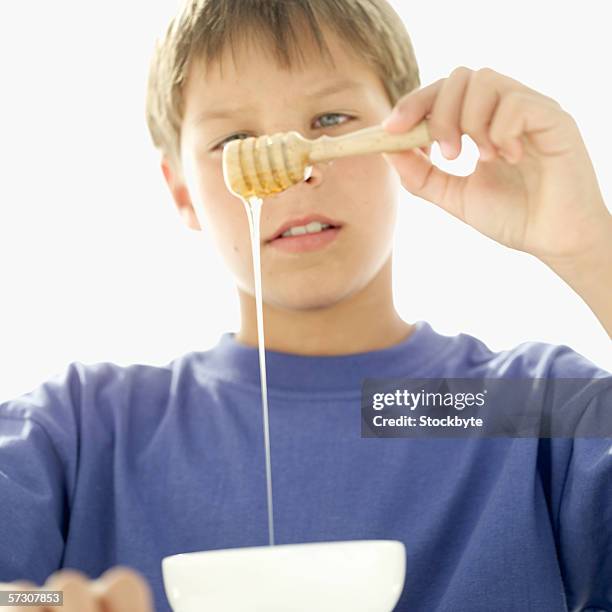 young boy (10-11) holding a honey dipper with honey over a bowl - tee reel stock pictures, royalty-free photos & images