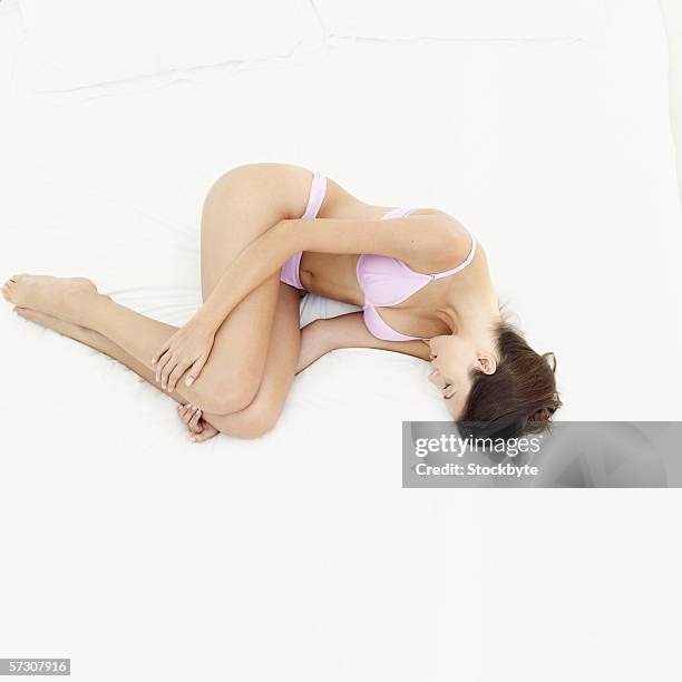 elevated side view of a young woman wearing underwear asleep on a bed - foetushouding stockfoto's en -beelden