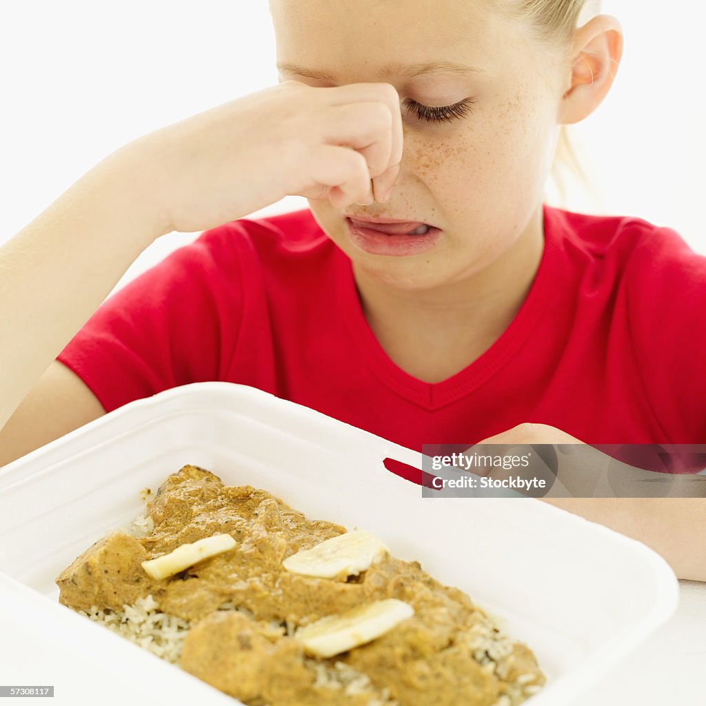 Young girl (8-9) holding her nose and looking down at gravy with rice and banana slices in a styrofoam pack