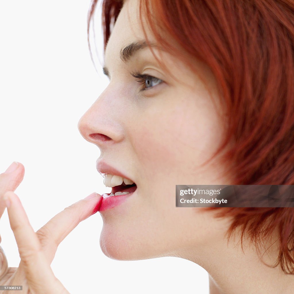 Side profile of a young woman applying lip gloss with finger