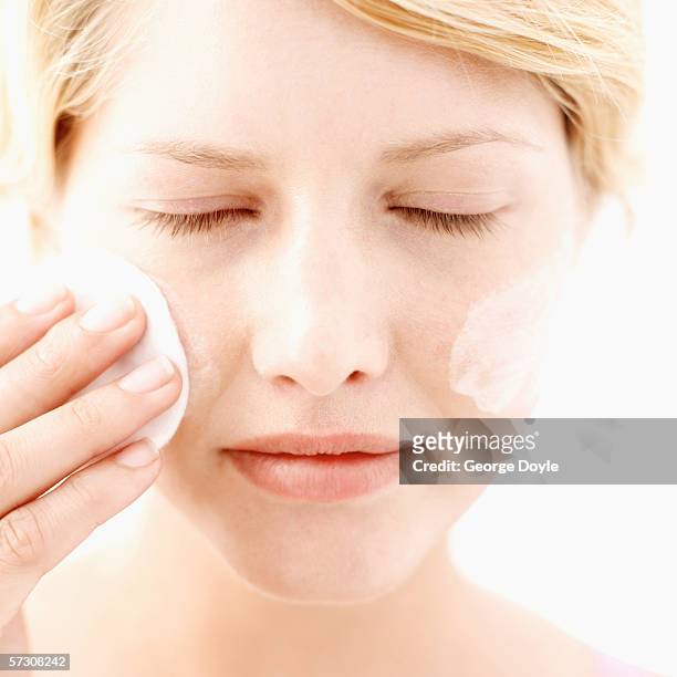 close-up of a young woman applying moisturizing lotion to her face using a cotton ball - woman applying cotton ball stock pictures, royalty-free photos & images