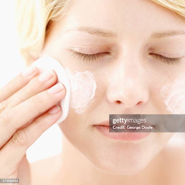 close-up of a young woman applying moisturizer to her face with cotton wool - woman applying cotton ball stock pictures, royalty-free photos & images