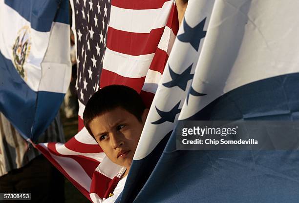 Nine-year-old Jonathan Reyes-Yanes of Washington peeks through the flags of El Salvador, the United States and Honduras while joining the tens of...