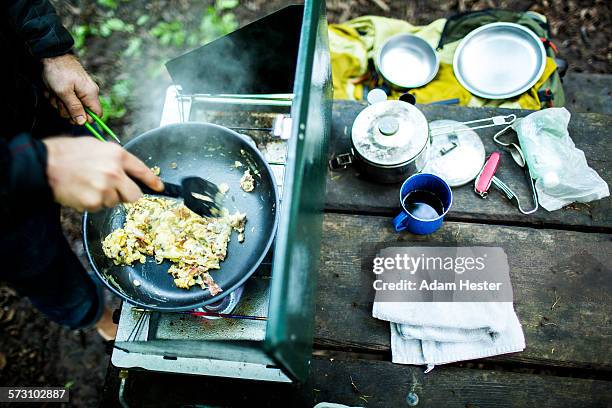 caucasian man cooking eggs at campsite - camping stove stockfoto's en -beelden