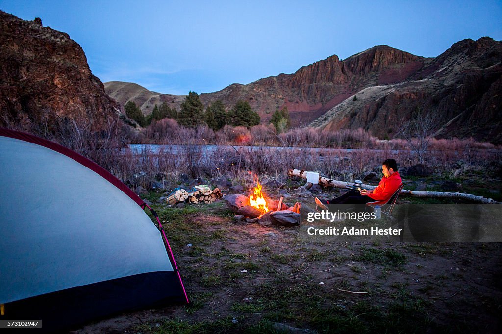 Caucasian hiker sitting near campfire in desert field, Painted Hills, Oregon, United States