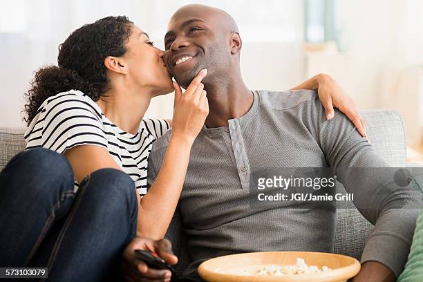 smiling couple watching television on sofa - black women kissing white men stock pictures, royalty-free photos & images
