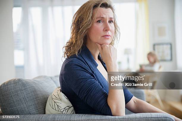 concerned caucasian woman sitting on sofa - woman concerned stockfoto's en -beelden