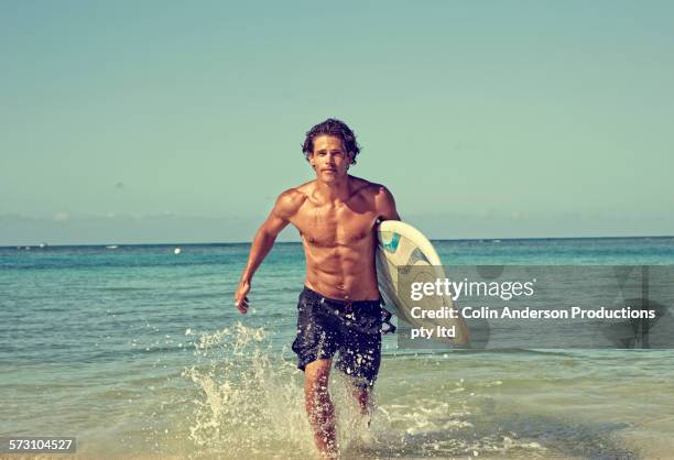 caucasian man carrying surfboard on beach - running shorts fotografías e imágenes de stock