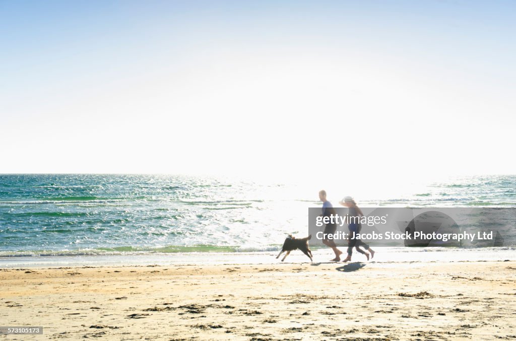 Caucasian family running with dog on beach