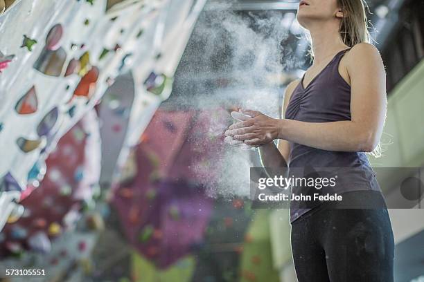 athlete chalking her hands at rock wall in gym - chalk rock stock-fotos und bilder