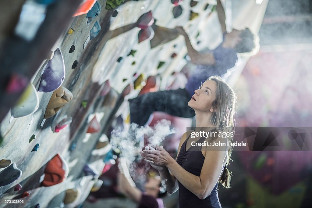 Athlete chalking her hands at rock wall in gym