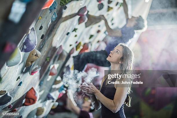 athlete chalking her hands at rock wall in gym - klimmuur stockfoto's en -beelden