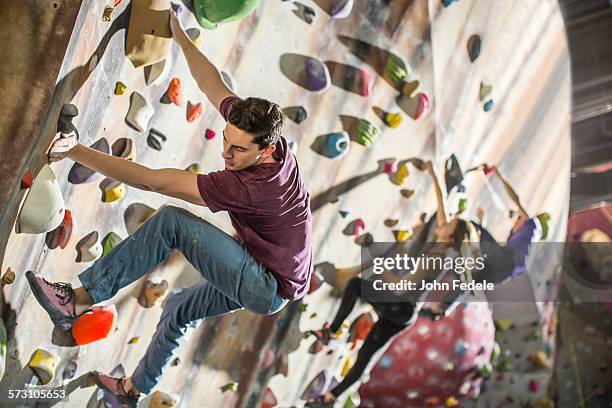 athletes climbing rock wall in gym - boulderen stockfoto's en -beelden