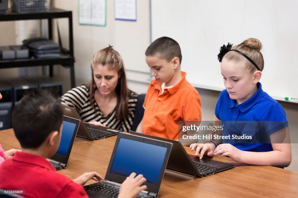 Teacher helping students use laptops in classroom