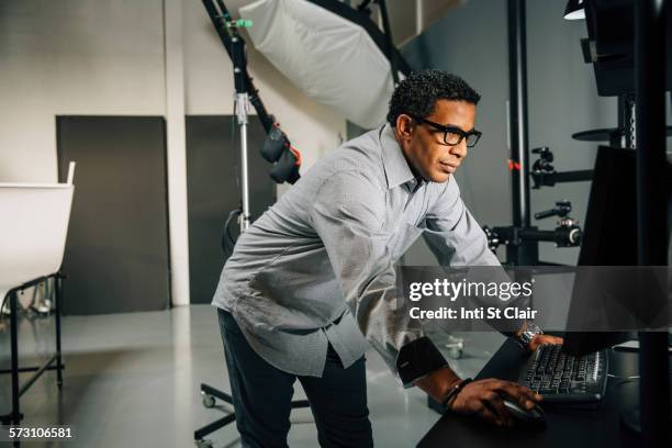 mixed race photographer using computer in studio - mixed race man standing studio stockfoto's en -beelden