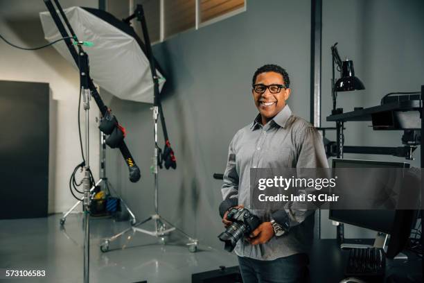 mixed race photographer holding camera in studio - mixed race man standing studio stockfoto's en -beelden