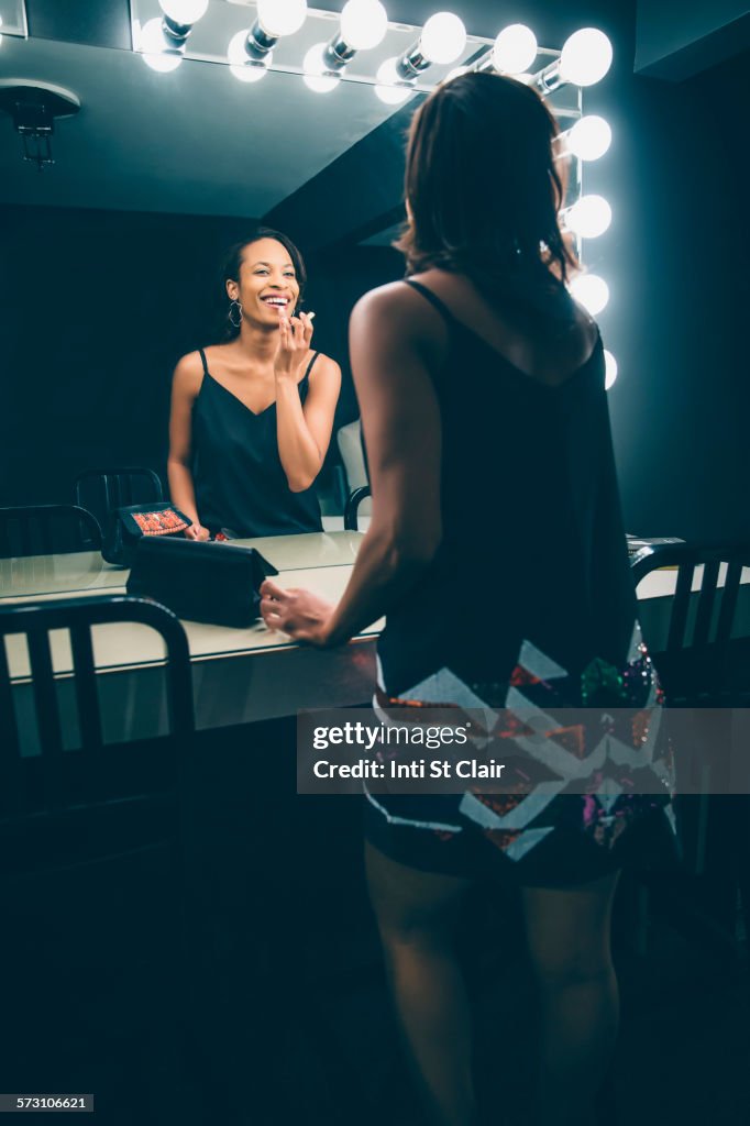 Black woman applying makeup in vanity mirror