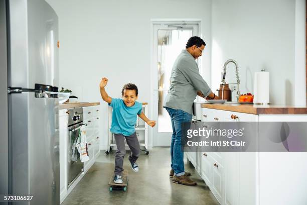boy skateboarding near father in kitchen - family chaos stock pictures, royalty-free photos & images